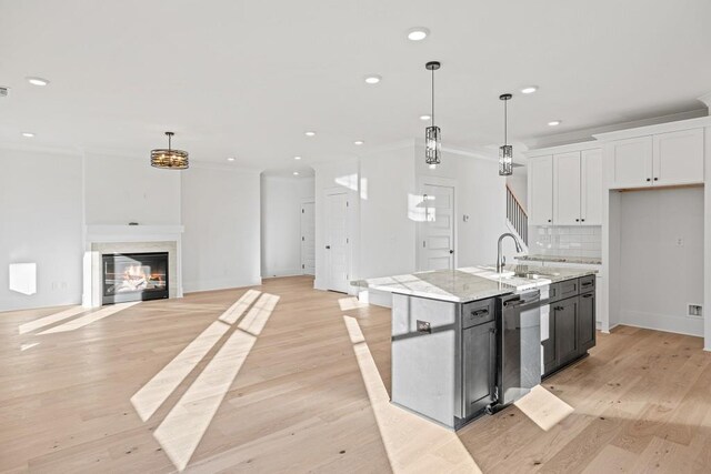 kitchen featuring white cabinetry, an island with sink, decorative light fixtures, light hardwood / wood-style floors, and backsplash