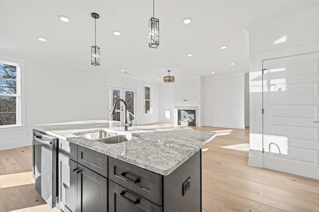 kitchen featuring stainless steel dishwasher, decorative light fixtures, a sink, and light wood finished floors
