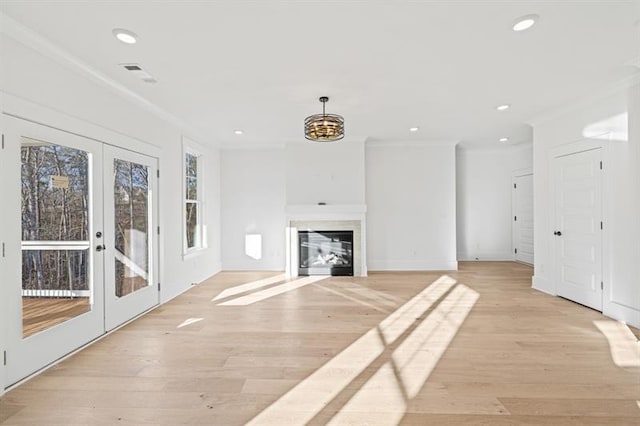 unfurnished living room featuring light wood-style floors, ornamental molding, french doors, and a glass covered fireplace