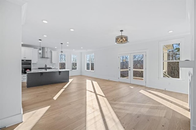 unfurnished living room featuring french doors, baseboards, light wood finished floors, a chandelier, and recessed lighting
