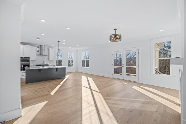 unfurnished living room with an inviting chandelier, light wood-type flooring, french doors, and sink