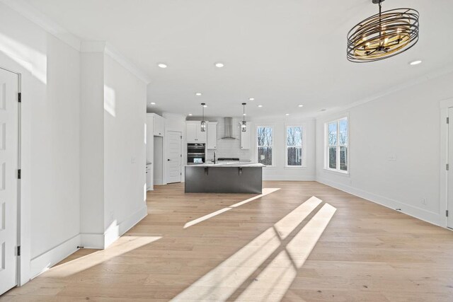 unfurnished living room featuring a notable chandelier, ornamental molding, and light wood-type flooring