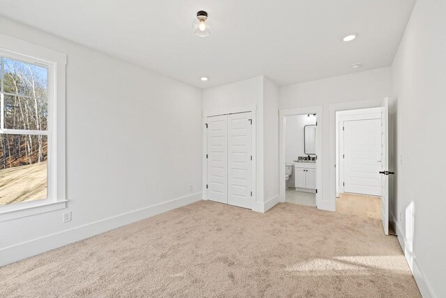 unfurnished bedroom featuring ensuite bath, light carpet, and a closet