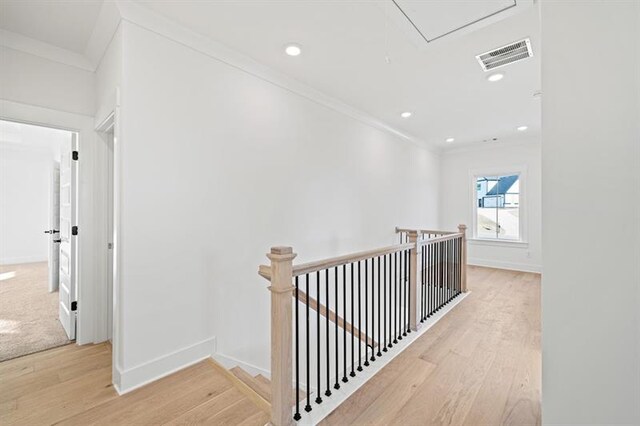 corridor featuring light wood-style floors, crown molding, visible vents, and an upstairs landing