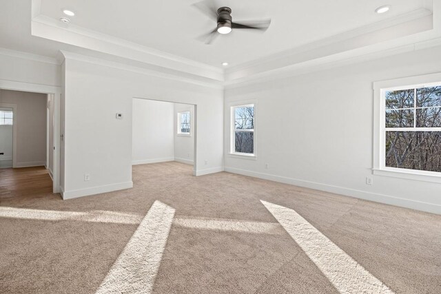 interior space with a tray ceiling, crown molding, light colored carpet, and ceiling fan