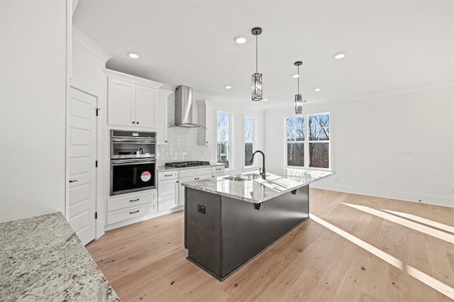 kitchen featuring wall chimney range hood, gas cooktop, stainless steel double oven, a sink, and recessed lighting