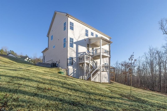 rear view of house with board and batten siding, a lawn, stairway, central AC, and a balcony