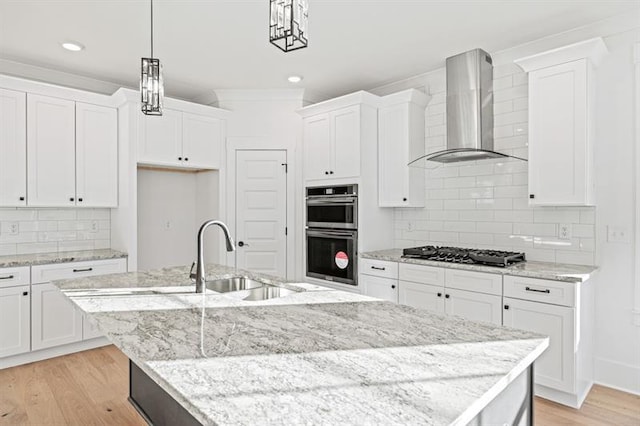 kitchen featuring gas cooktop, double oven, a kitchen island with sink, wall chimney exhaust hood, and white cabinetry