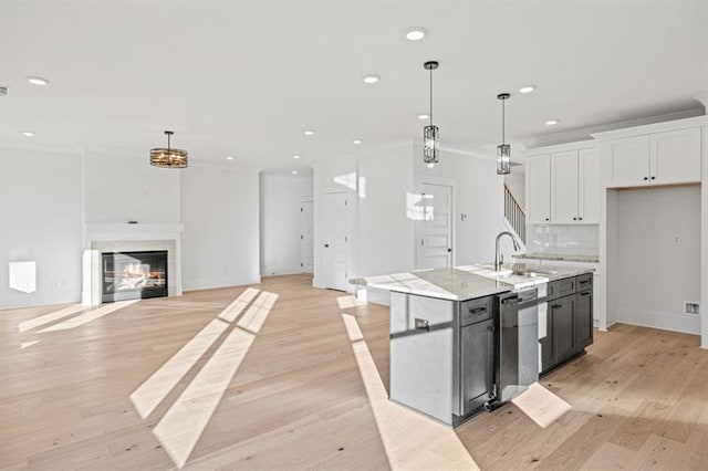 kitchen with white cabinets, crown molding, hanging light fixtures, a sink, and a center island with sink