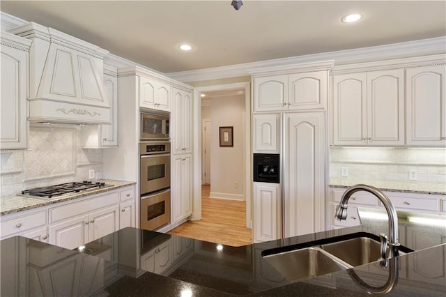 kitchen with custom exhaust hood, white cabinetry, backsplash, and built in appliances