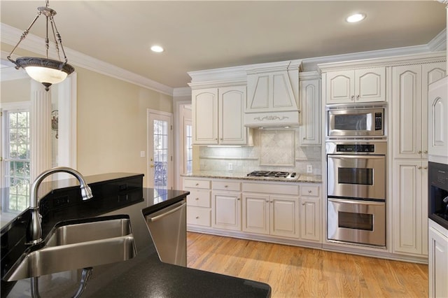 kitchen featuring crown molding, stainless steel appliances, light wood-style floors, a sink, and premium range hood