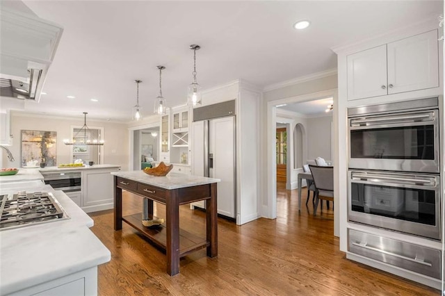 kitchen with a warming drawer, stainless steel appliances, ornamental molding, light countertops, and white cabinetry