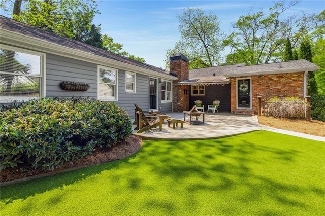 rear view of house with a chimney, a lawn, and a patio