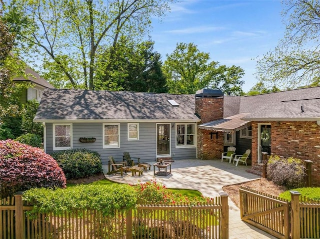 rear view of house featuring a patio area, a fire pit, a chimney, and fence