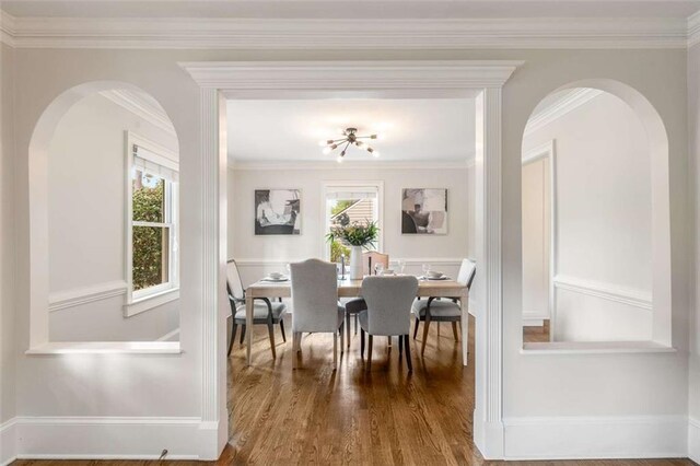 dining room featuring arched walkways, wood finished floors, crown molding, and baseboards