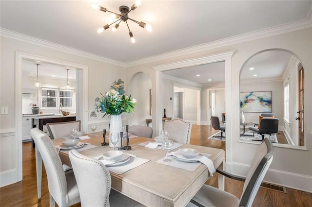 dining area featuring arched walkways, a chandelier, wood finished floors, crown molding, and baseboards