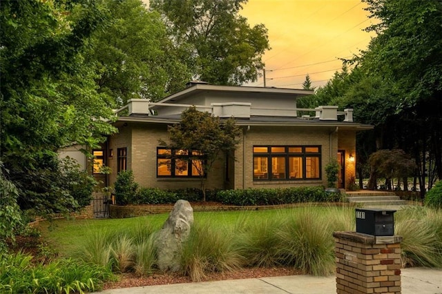 back of house at dusk featuring brick siding