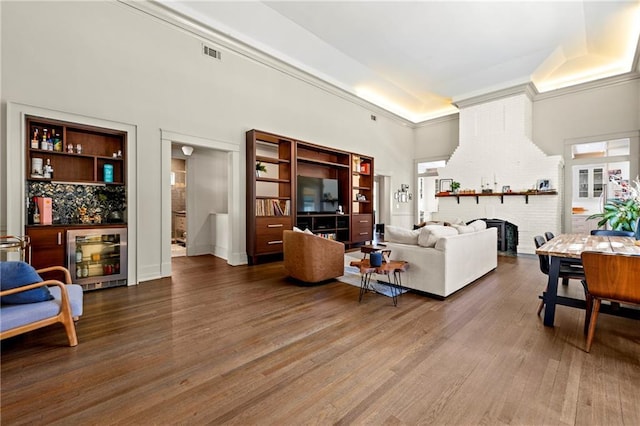 living room featuring wood finished floors, visible vents, wine cooler, a brick fireplace, and a dry bar