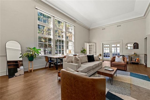 living area with a high ceiling, wood finished floors, visible vents, and baseboards