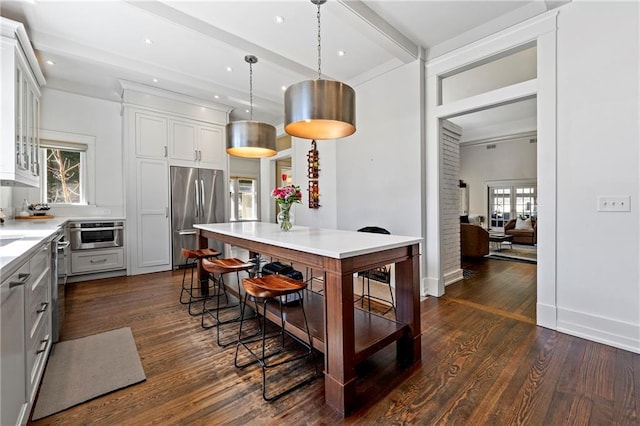 kitchen featuring dark wood finished floors, beamed ceiling, pendant lighting, light countertops, and appliances with stainless steel finishes