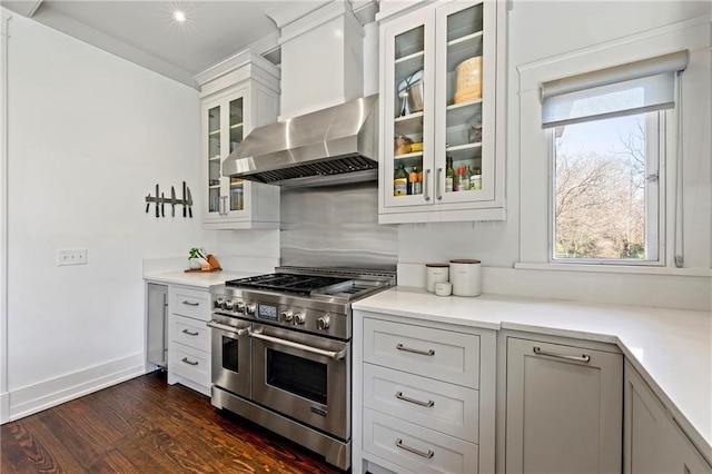 kitchen with glass insert cabinets, dark wood finished floors, light countertops, range with two ovens, and wall chimney exhaust hood