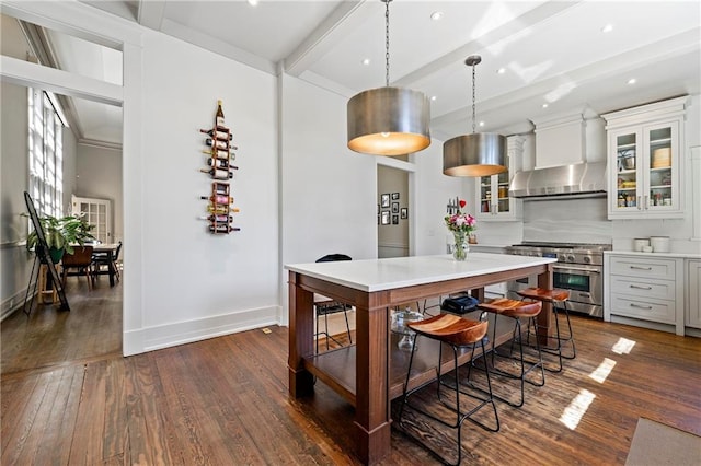 kitchen featuring wall chimney range hood, beamed ceiling, light countertops, stainless steel stove, and dark wood-style flooring