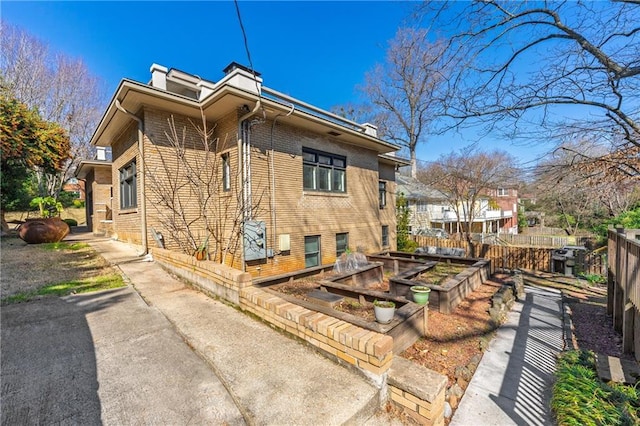 view of property exterior featuring a vegetable garden, fence, brick siding, and a chimney