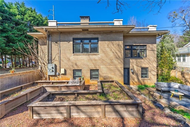 back of property featuring brick siding, an outdoor living space, and a vegetable garden