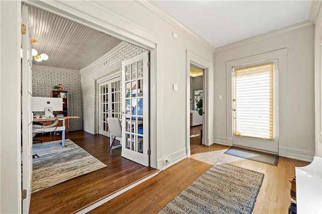 foyer entrance featuring french doors, wood finished floors, brick wall, and ornamental molding