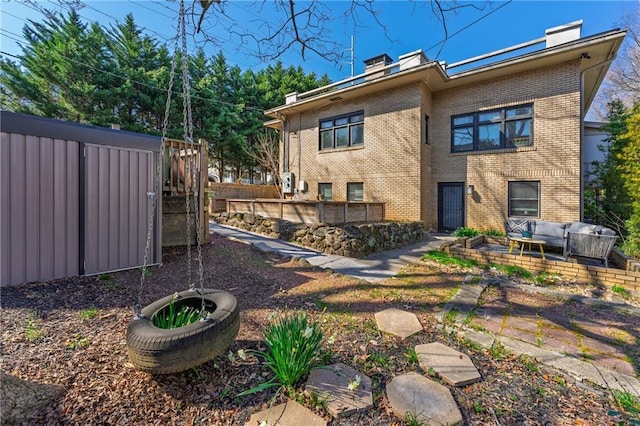 back of property featuring an outdoor hangout area, brick siding, a chimney, and fence