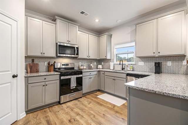 kitchen with appliances with stainless steel finishes, light stone countertops, sink, and gray cabinetry