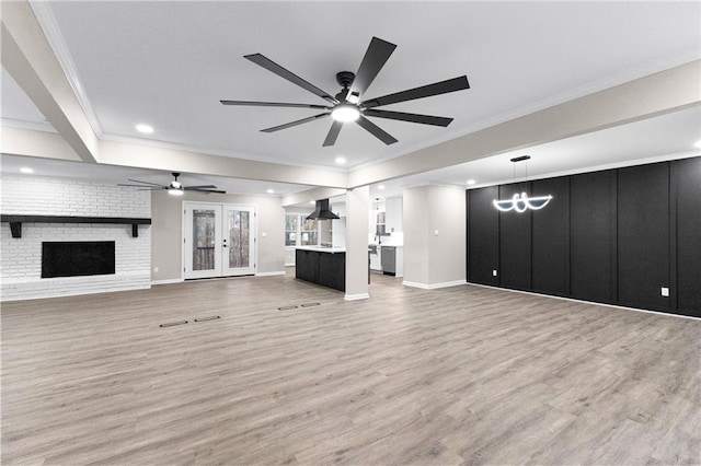 unfurnished living room featuring ceiling fan with notable chandelier, hardwood / wood-style floors, french doors, and a fireplace