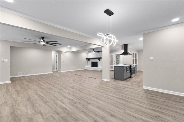 unfurnished living room featuring a brick fireplace, light hardwood / wood-style flooring, ornamental molding, and ceiling fan with notable chandelier