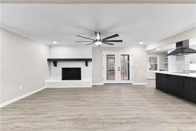 unfurnished living room featuring a brick fireplace, light hardwood / wood-style floors, ornamental molding, and french doors