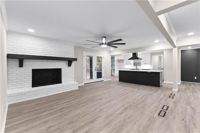 unfurnished living room with a fireplace, light wood-type flooring, french doors, ornamental molding, and ceiling fan