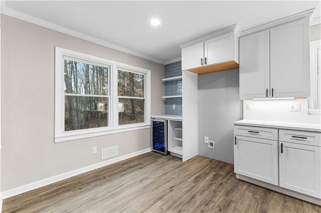 kitchen featuring crown molding, light hardwood / wood-style flooring, wine cooler, backsplash, and white cabinetry