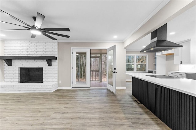 kitchen with white cabinetry, island exhaust hood, ornamental molding, a brick fireplace, and black electric cooktop