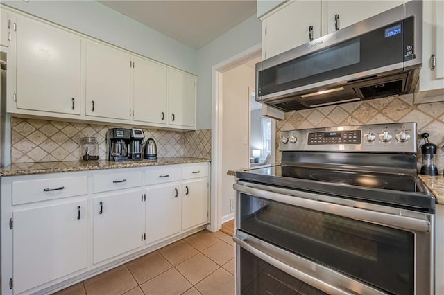 kitchen with light tile patterned floors, light stone counters, appliances with stainless steel finishes, white cabinetry, and backsplash