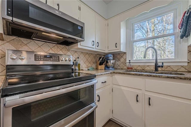 kitchen with light stone countertops, a sink, appliances with stainless steel finishes, white cabinetry, and backsplash