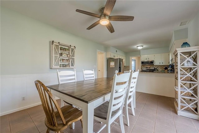 dining area featuring light tile patterned floors, visible vents, a ceiling fan, and wainscoting