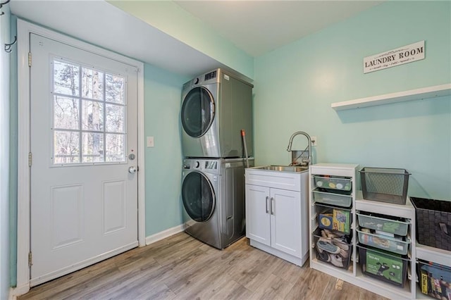 laundry room featuring baseboards, cabinet space, a sink, stacked washer and dryer, and light wood-type flooring