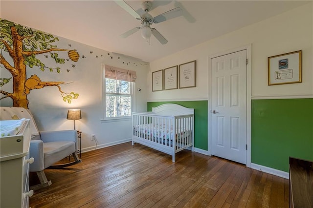 bedroom with baseboards, a nursery area, a ceiling fan, and hardwood / wood-style flooring