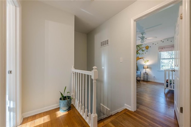 hallway with hardwood / wood-style flooring, an upstairs landing, visible vents, and baseboards