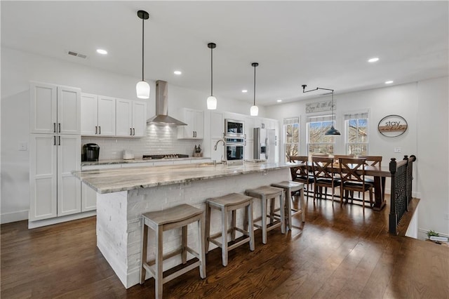 kitchen with dark wood-style flooring, stainless steel appliances, tasteful backsplash, visible vents, and wall chimney range hood