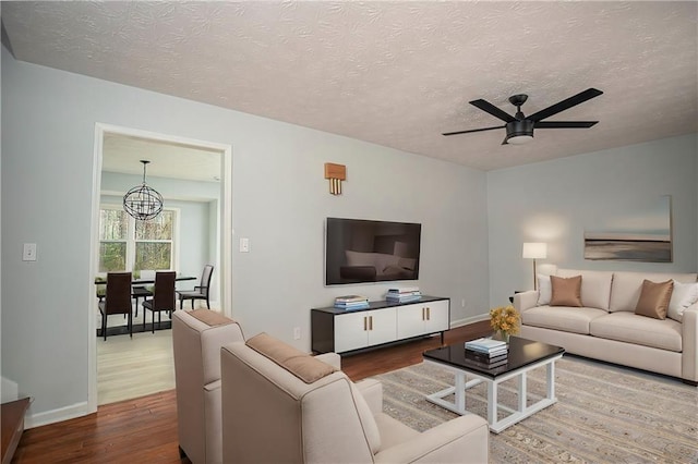 living room with ceiling fan with notable chandelier, a textured ceiling, and wood finished floors