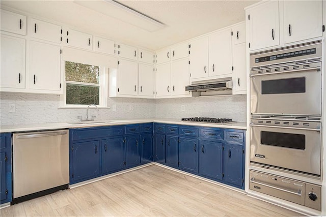 kitchen with under cabinet range hood, blue cabinetry, stainless steel appliances, and a sink