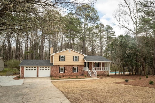 tri-level home featuring an attached garage, covered porch, brick siding, concrete driveway, and a chimney