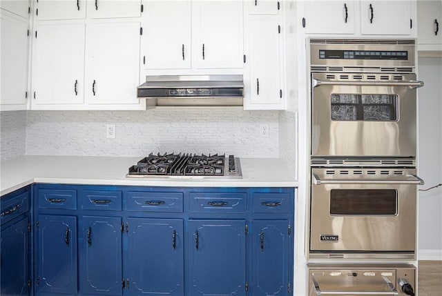 kitchen featuring stainless steel appliances, wall chimney range hood, light countertops, and blue cabinets