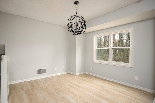 empty room with an inviting chandelier, wood finished floors, visible vents, and baseboards