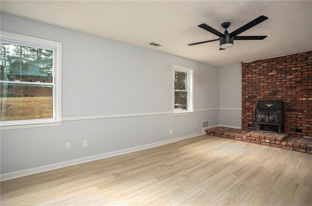 unfurnished living room with a wood stove, a textured ceiling, visible vents, and wood finished floors